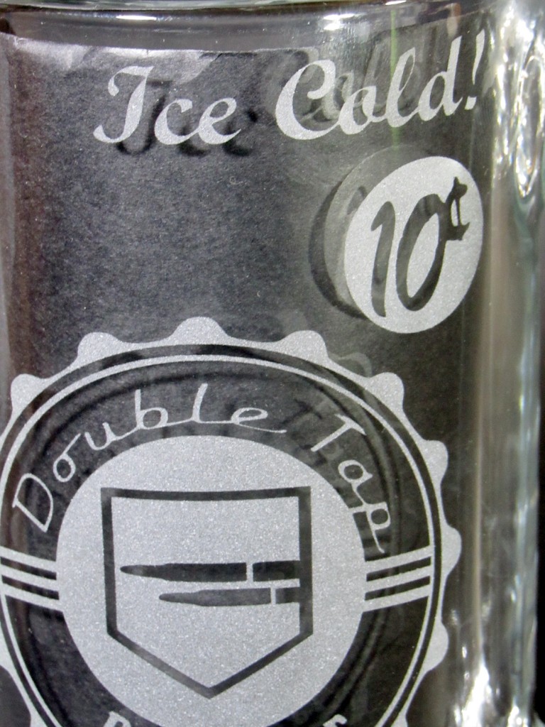 Close-up view of the Double Tap Mug design featuring: the words "Ice Cold", a "10 cents" circular price tag. and a logo featuring 2 speeding bullets